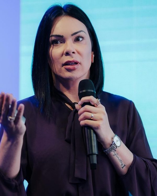Mila Estuqui apresentando no palco, microfone em mãos